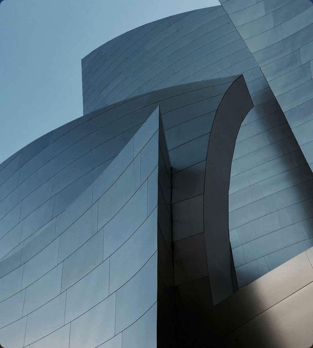 Abstract architectural structure featuring curved metallic surfaces and sharp angles against a clear blue sky.