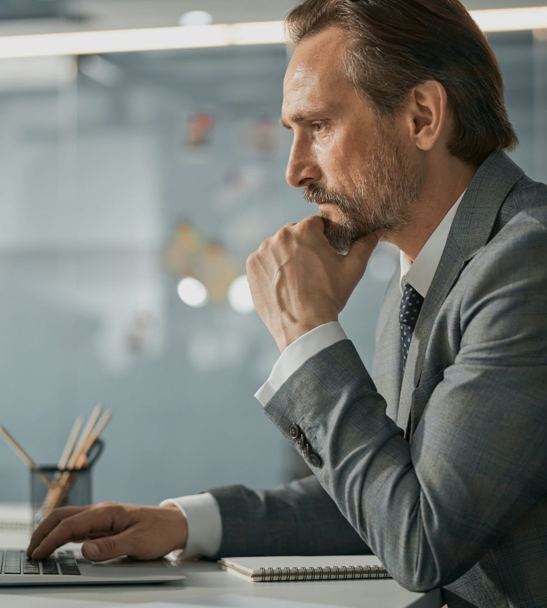 Business professional deep in thought while working on a laptop in a modern office setting.