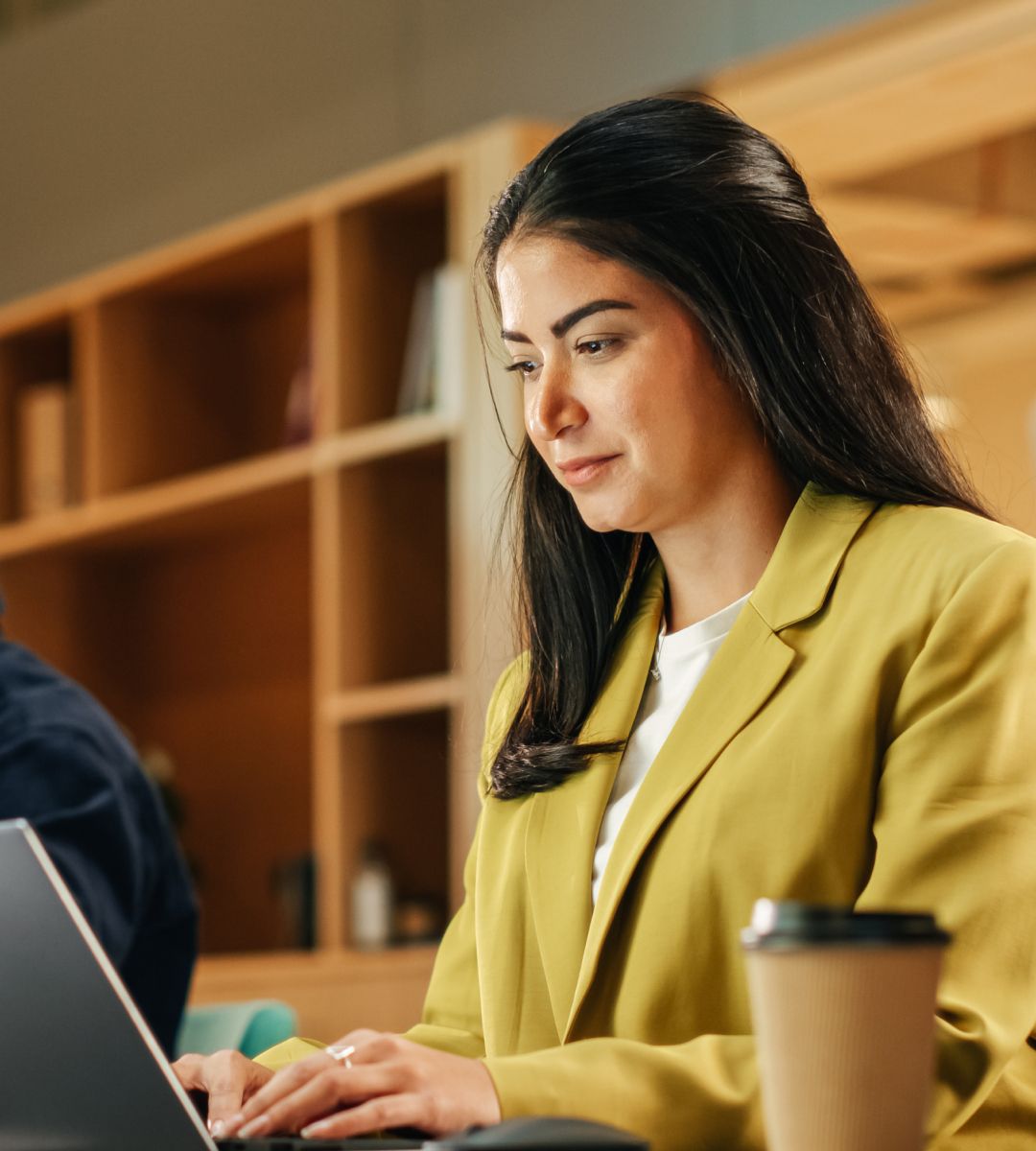 Professional working at a laptop in a modern office space with a coffee cup nearby.