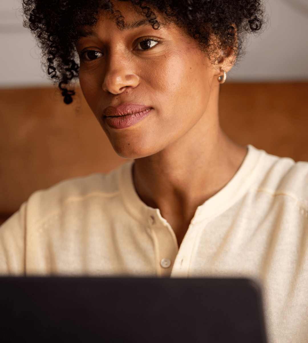 Close-up of a person focused on using a laptop, with a cozy indoor setting in the background.