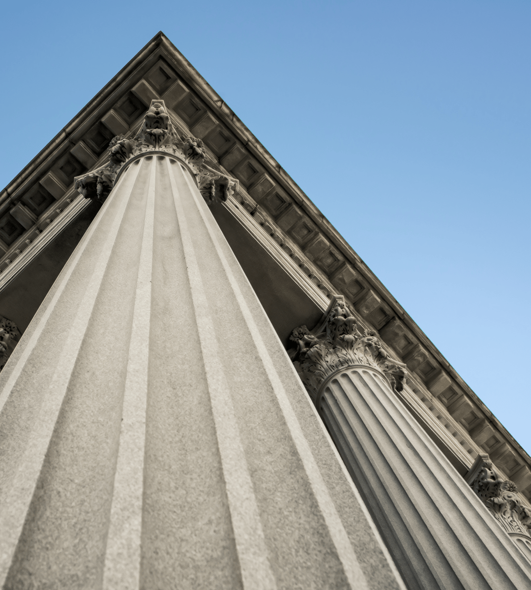 A low-angle view of classical columns with decorative capitals against a clear blue sky.