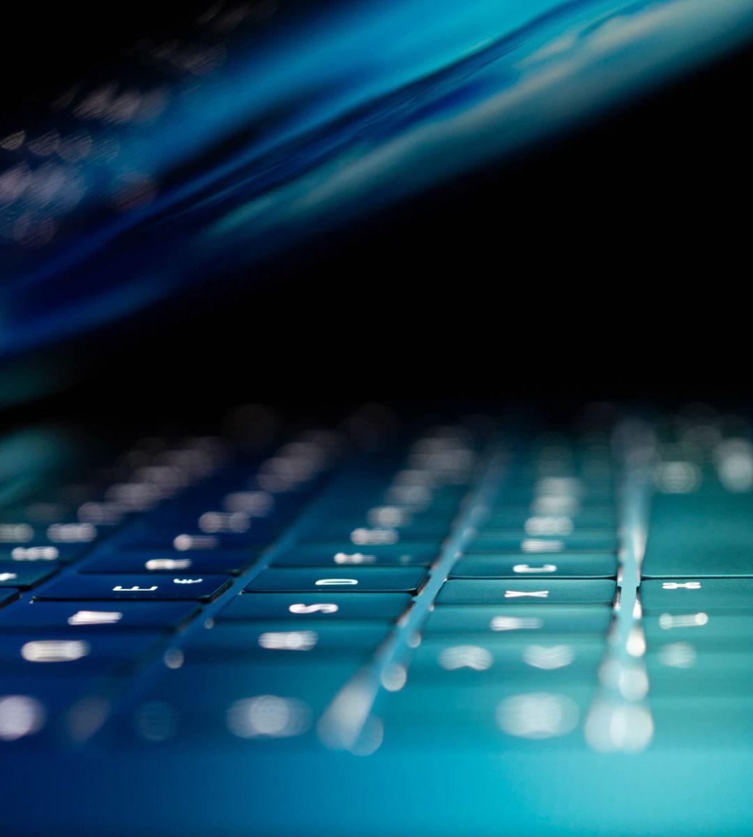 Close-up of a blue-lit keyboard with a blurred background, highlighting the keys and subtle lighting effects.