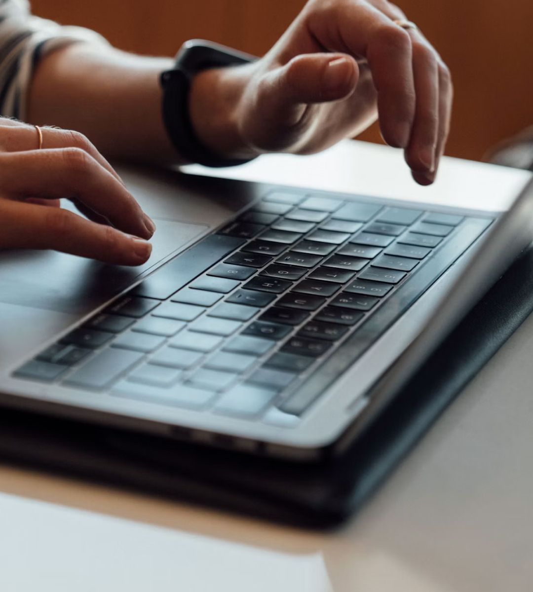 Hands typing on a laptop keyboard on a desk, with a focus on the device's black keyboard and a portion of the hands.