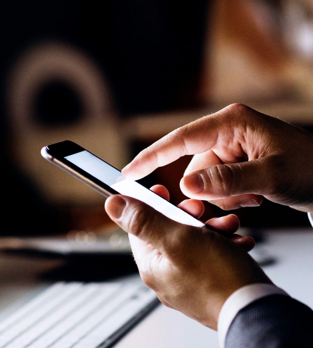 A close-up view of hands using a smartphone, with a faint light screen visible, set against a blurred background.