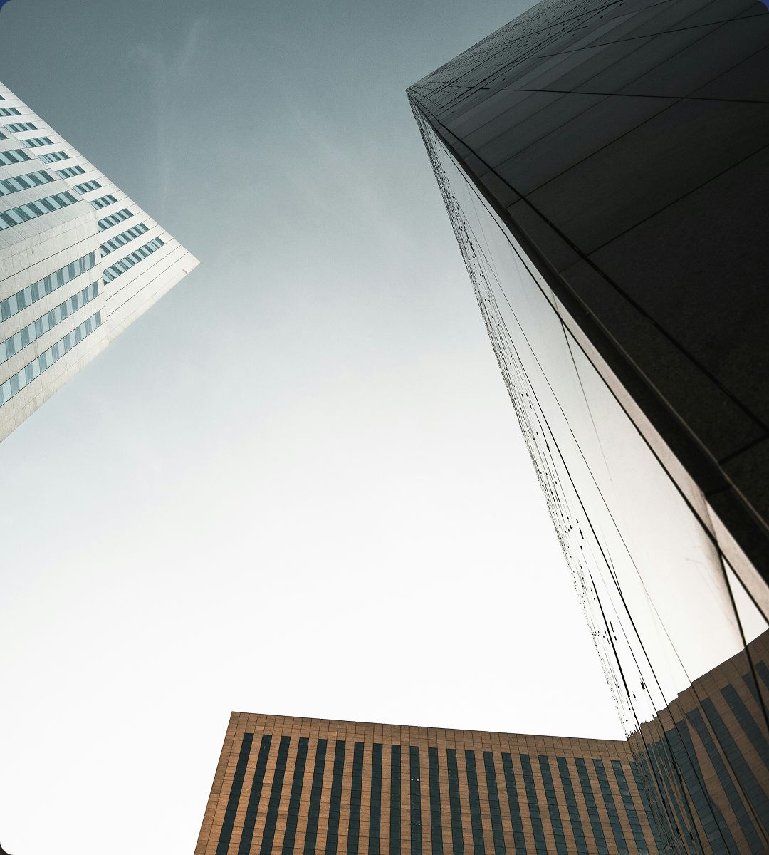 Skyward view of modern skyscrapers with glass façades, showcasing geometric patterns and a clear sky in the background.
