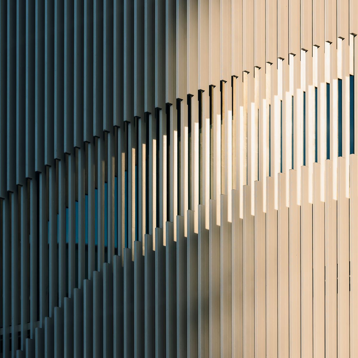 Architectural detail featuring a series of vertical slats with varying widths and colors, creating a dynamic play of light and shadow.