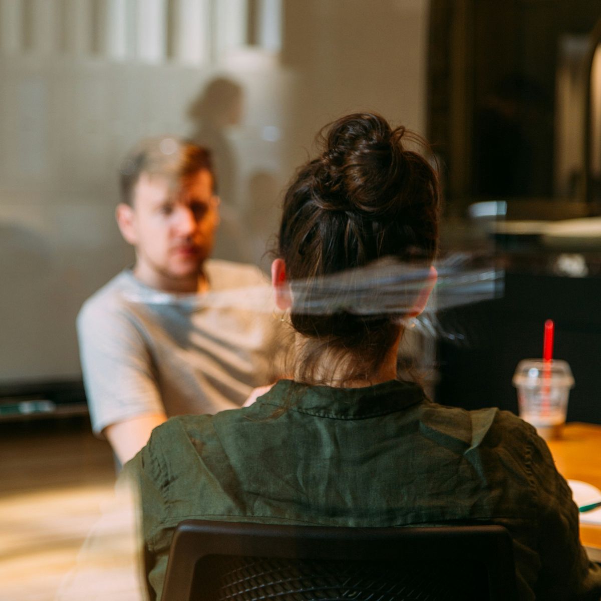 Two individuals engaged in a discussion, with one person partially obscured in the foreground and the other visible in the background.