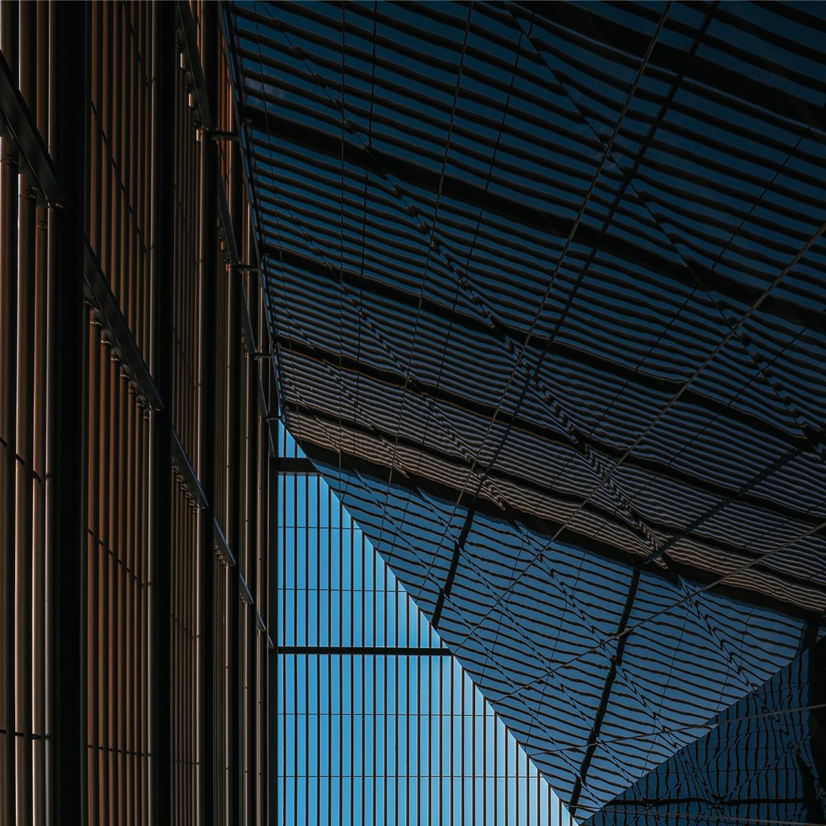 Architectural details featuring angular lines and shadows created by a glass structure against a clear blue sky.