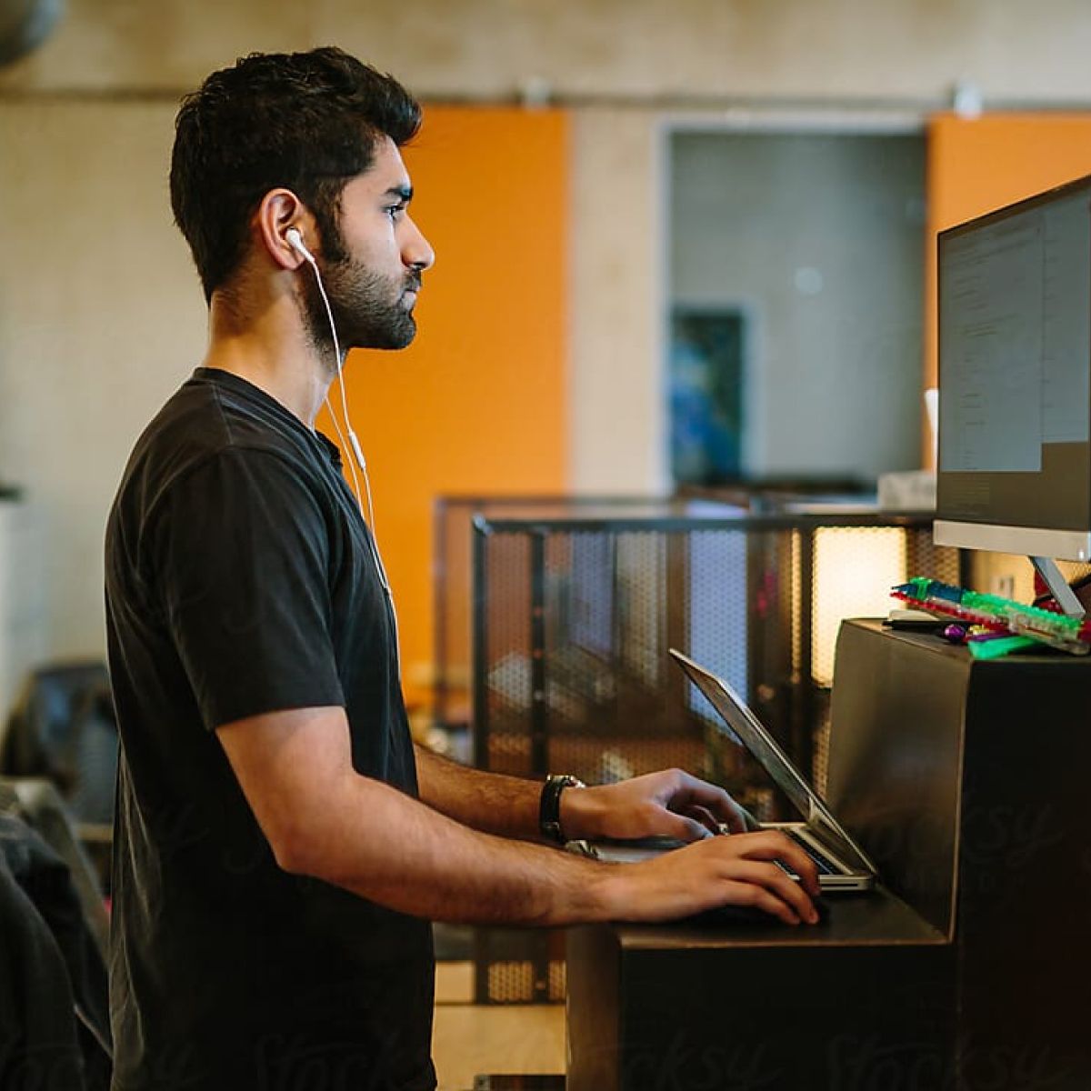 Person standing and working on a laptop with headphones, focused in a modern office environment with a blurred background.