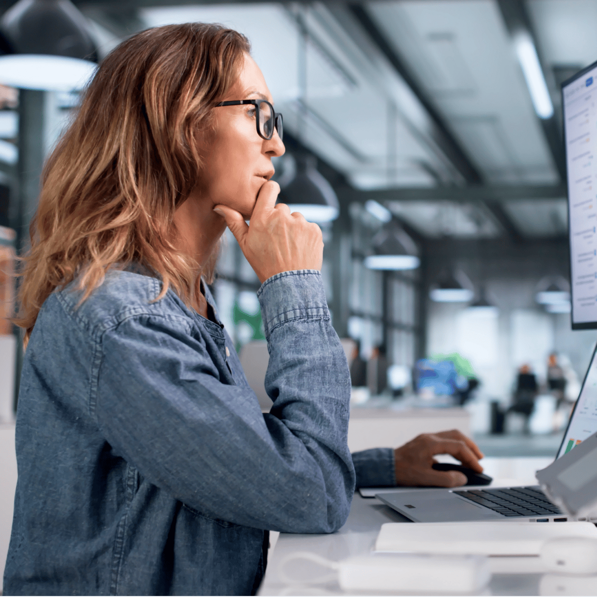 Person thoughtfully working at a computer in a modern office environment with bright lighting and contemporary furnishings.