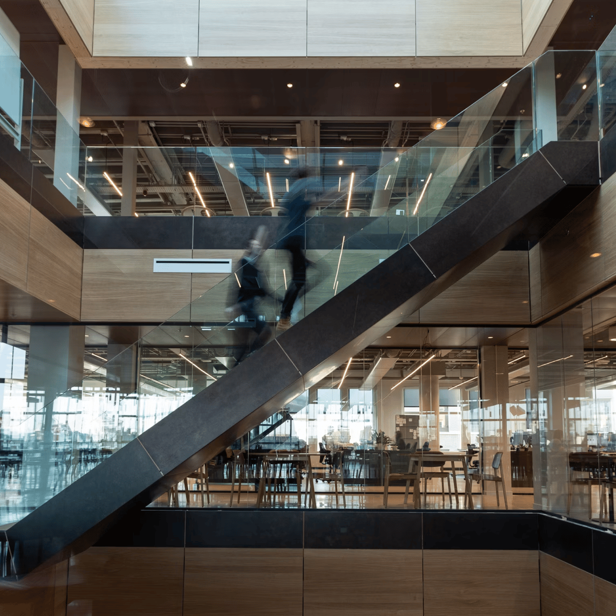 Blurred figure ascending a modern staircase in a stylish, open-concept space with wooden elements and glass panels.