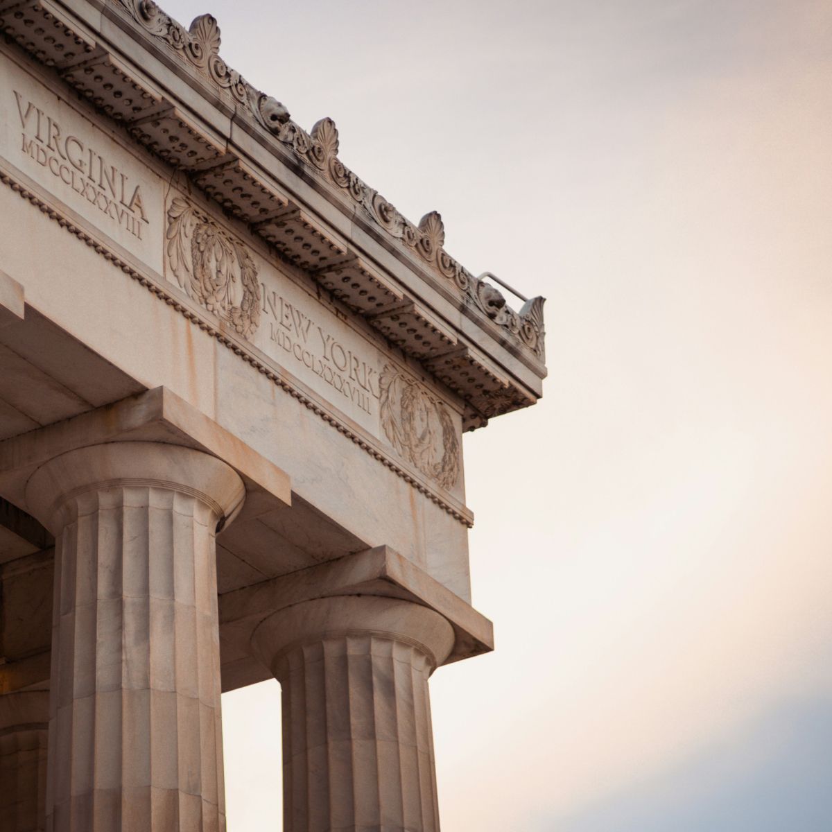 Ancient-style columns supporting a decorated structure with inscriptions for "VIRGINIA" and "NEW YORK" against a soft sky background.