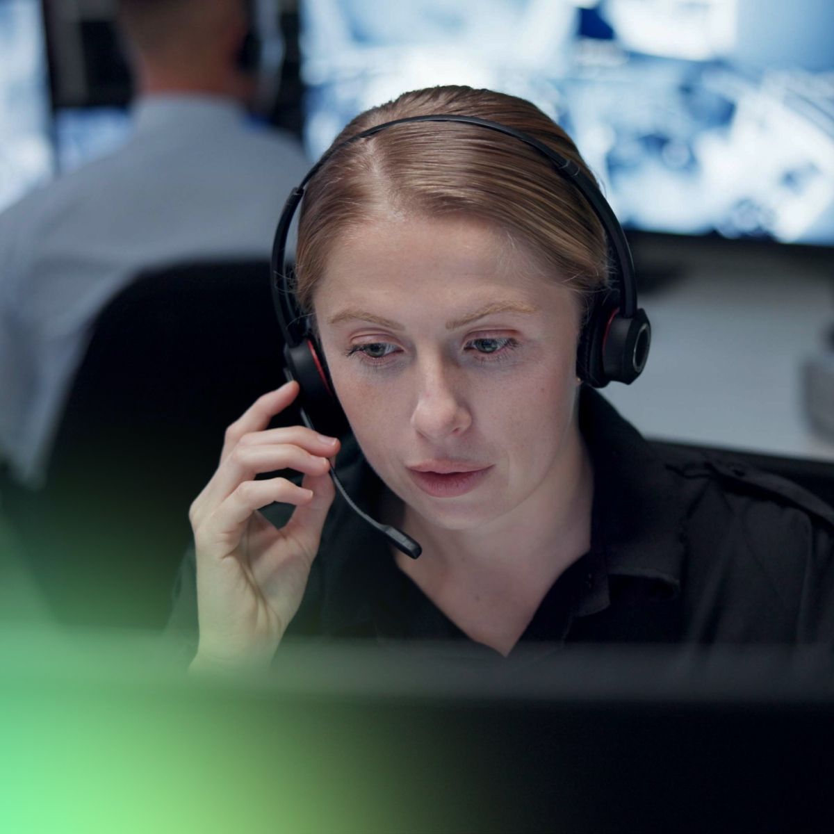A person wearing a headset is focused on a computer screen while communicating, with blurred figures in the background.