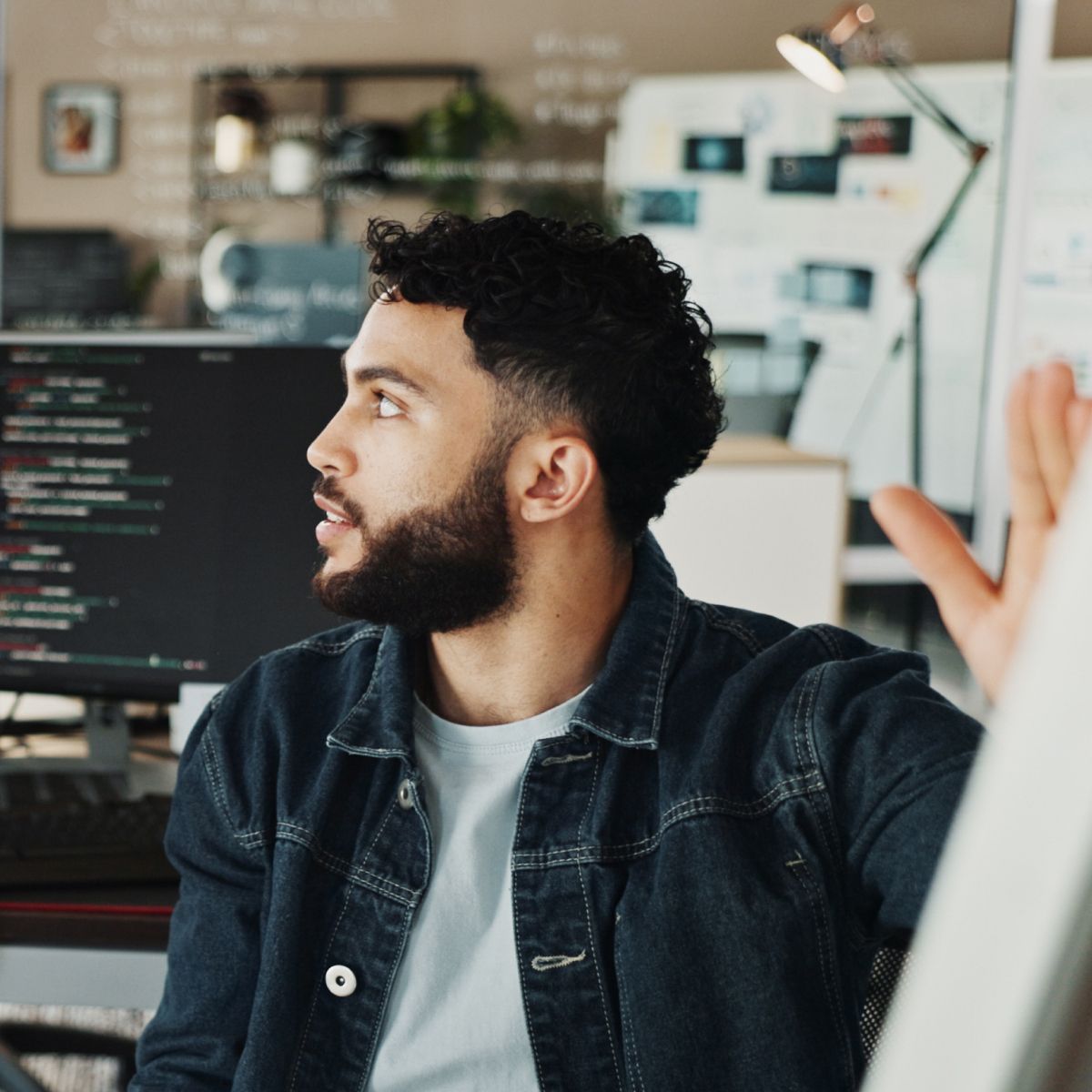 Person engaged in a discussion in a modern office setting, with computer code displayed on a screen in the background.