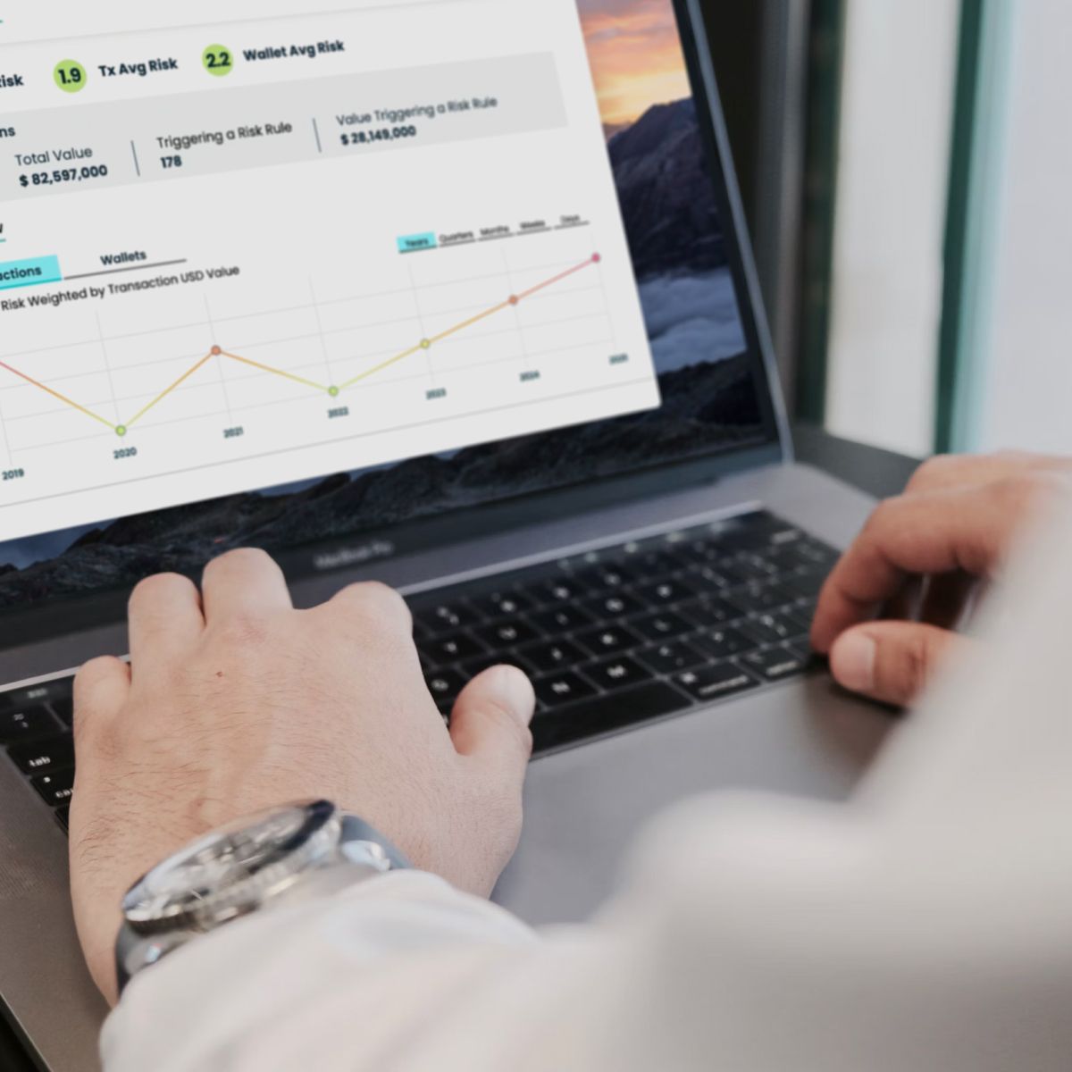 Laptop displaying cryptocurrency analytics with data on transaction and wallet average risk, alongside a line graph and financial metrics.