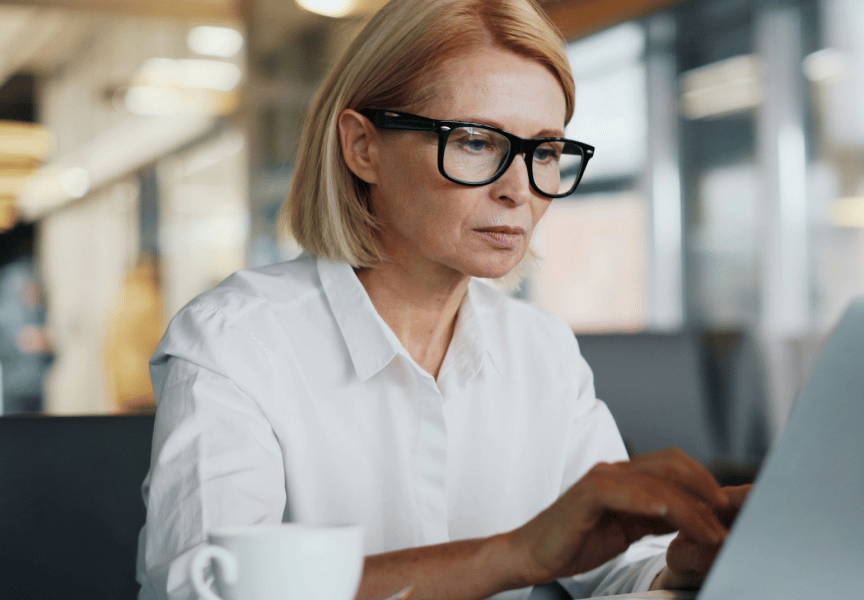 A focused individual working on a laptop in a modern office setting, with a cup of coffee on the table.