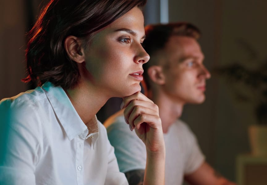 Two individuals focused on their work, with one resting their chin on their hand in contemplation, likely engaged in a creative task.