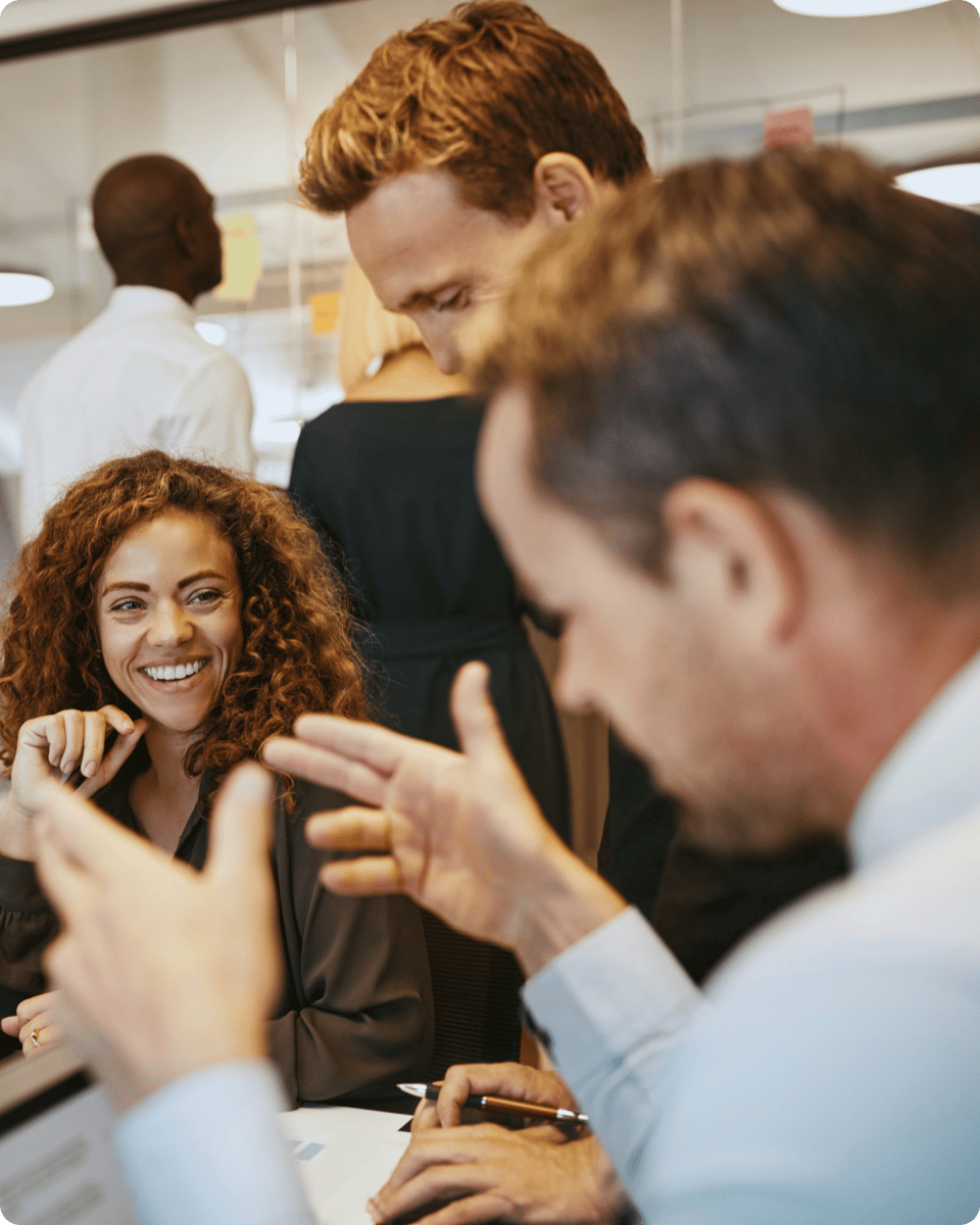 A group of people in a modern office setting, engaging in conversation, with one individual smiling and showing enthusiasm.