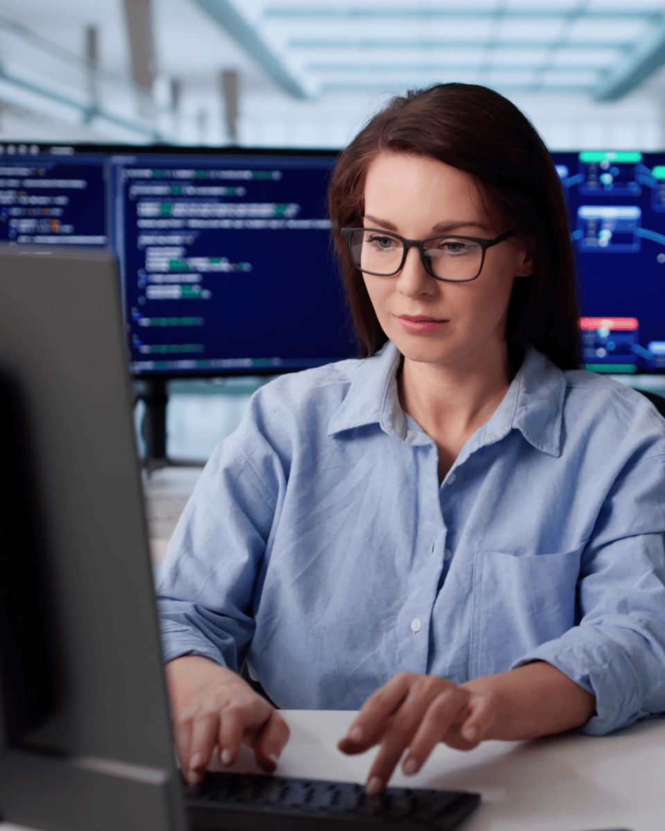 Person working on a computer with multiple screens displaying code and data in a modern office environment.