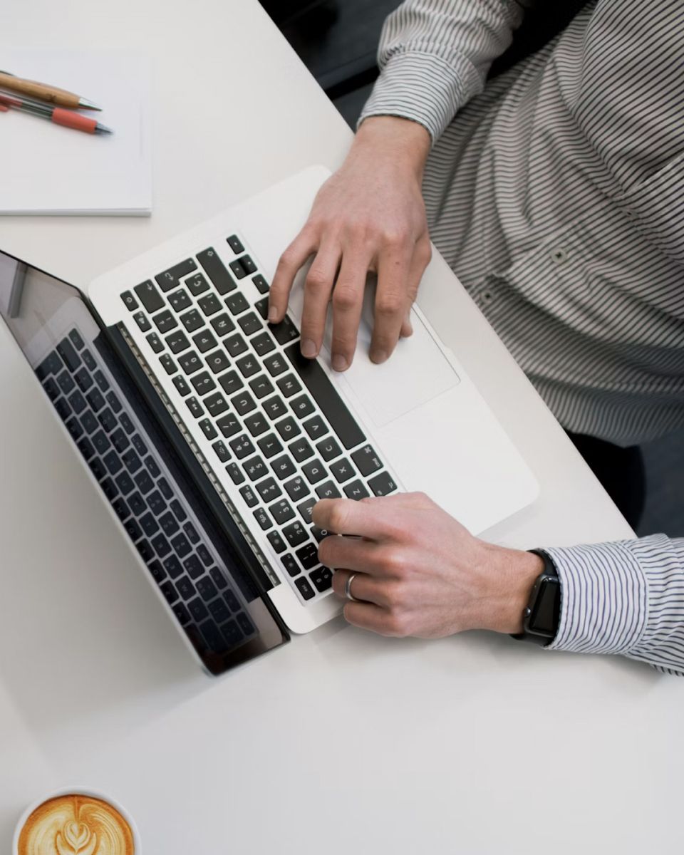 A workspace featuring a laptop, a person's hands typing, and a cup of coffee on a table.