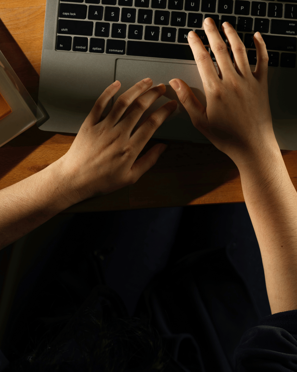 Two hands typing on a laptop keyboard, viewed from above, with a dimly lit background and a soft focus.