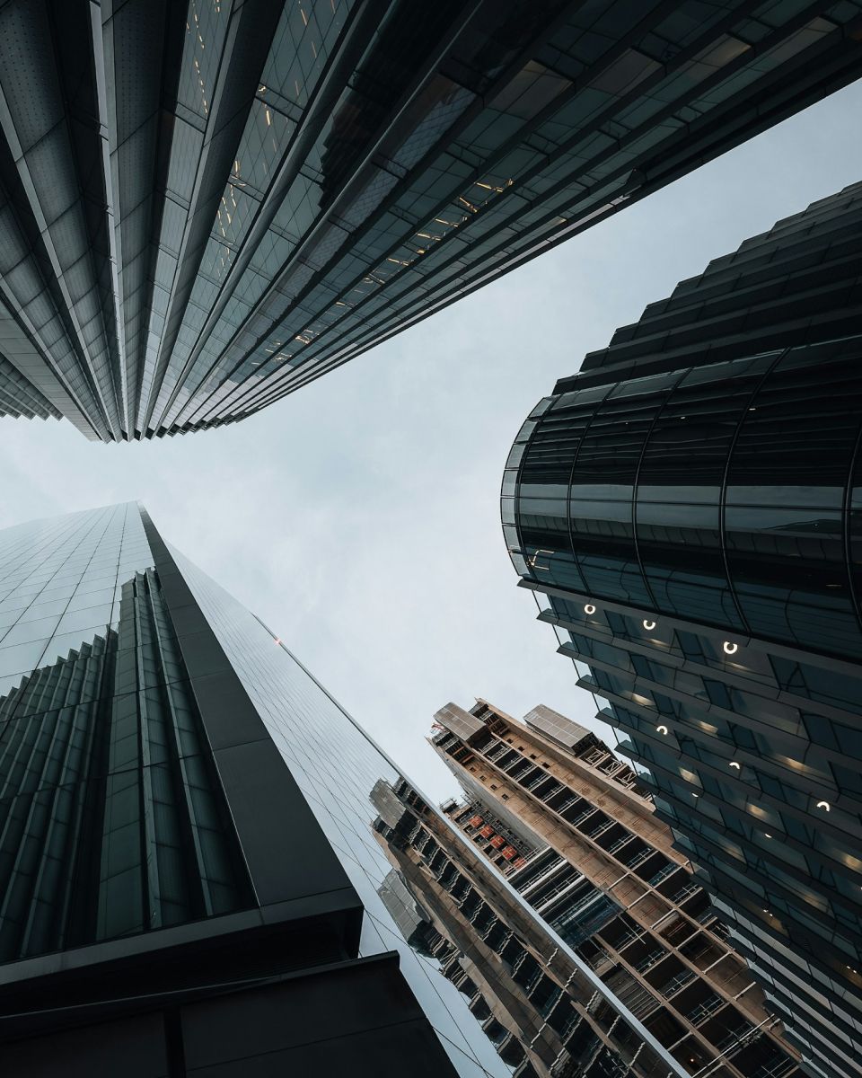 Skyscrapers viewed from below, showcasing a mix of glass and steel structures against a cloudy sky.