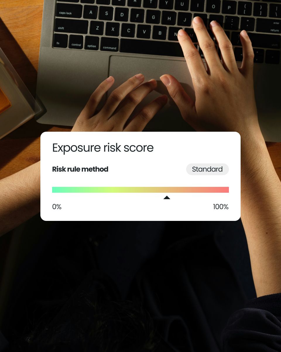 Hands on a laptop keyboard with a display showing an exposure risk score, indicating a gradual scale from 0% to 100% and a standard risk rule method.